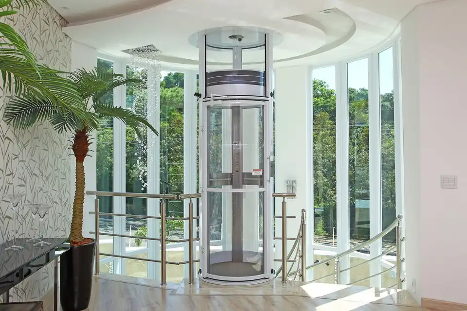 Elevador residencial panorâmico instalado em uma residência clara, ao lado de grandes janelas