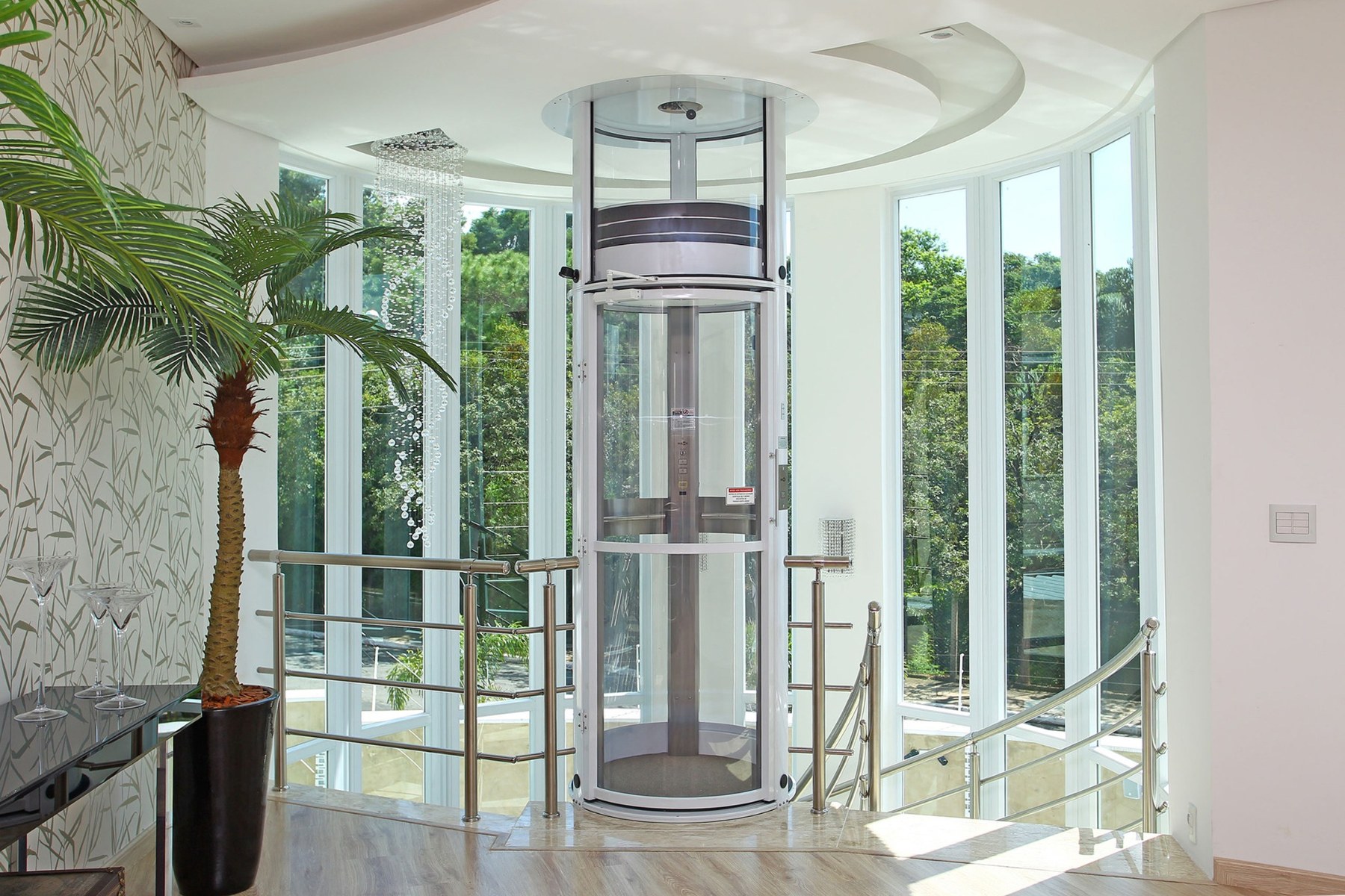 Elevador residencial panorâmico instalado em uma residência clara, ao lado de grandes janelas