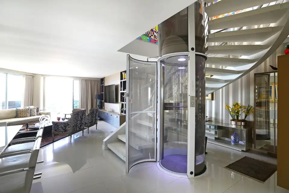 Elevador residencial com porta aberta integrado a uma sala e à escada existente